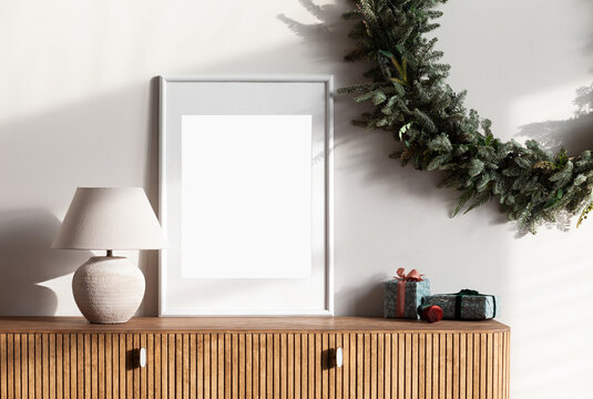 Blank picture frame mockup on white wall. Stylish Christmas decoration in modern interior design with artwork mock up. Merry Christmas and Happy Holidays. Template.