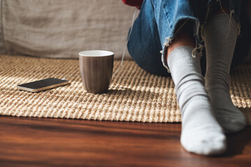 Closeup of a young woman sitting in living room with mobile phone and coffee cup on the floor