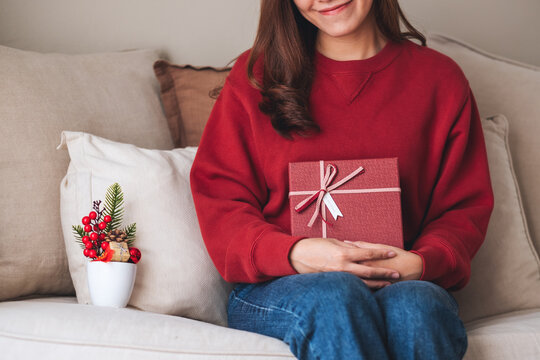 Closeup image of a young woman holding a red present box at home