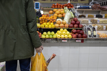 Adult man choosing buying fresh fruits at market and holding package with mutton meat. Food shopping concept.