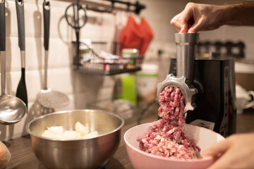 Mincer machine with fresh chopped meat at home kitchen. Preparing ground meat male hands closeup.