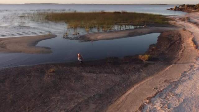 Aerial orbit shot of person taking pictures of beautiful landscape with sandy islands, lake shore of Laguna Negra during sunset in Uruguay