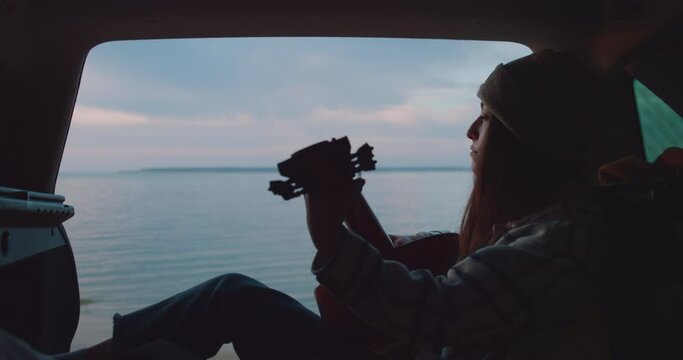 Dolly in shot of a sad remorseful woman regretting and heartbroken playing her guitar in the back of the car