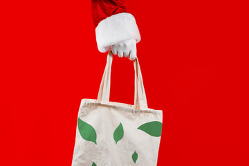 String bag with eco pattern in Santa's hands on a red background. Sale, contactless ,holidays concept.