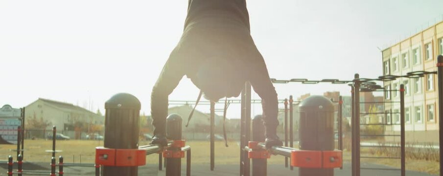Zoom in shot of athletic man in sportswear doing handstand on parallel bars at workout playground