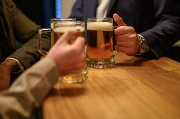 Cheerful colleagues drinking beer in the bar together after work and using a tablet