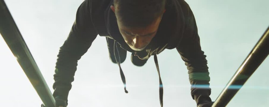 Low angle shot of male athlete in sporswear doing handstand on parallel bars outdoor