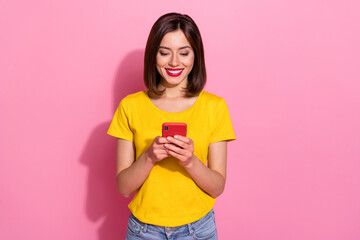 Photo of sweet charming young woman wear yellow outfit typing modern device smiling isolated pink...