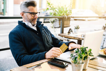 Business man holding credit card and using laptop sitting at coffee bar table - Man trader investor...