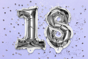 Silver foil balloon number, digit eighteen on a lilac background with sequins. Birthday greeting card with inscription 18. Anniversary concept. Top view. Numerical digit. Celebration event, template.
