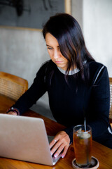 Image of happy woman using laptop while sitting at cafe. Young caucasian woman sitting in a coffee shop