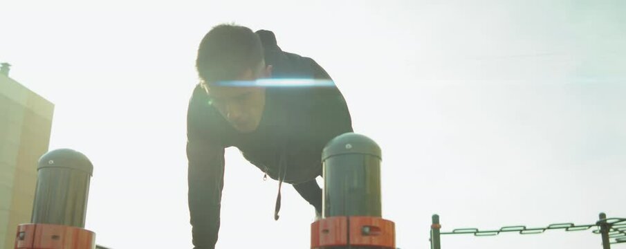 Arc shot of young athlete in sportswear doing full planche on parallel bars while training outdoors at workout playground
