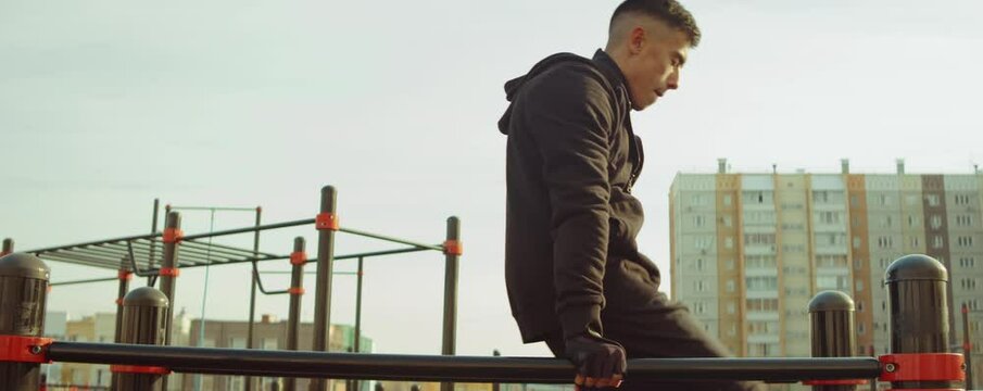 Arc shot of sportsman doing straddle planche on parallel bars while training outdoors at workout playground