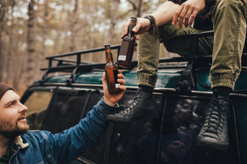 Two millennial man hiking in a forest, drinking beer and having fun.