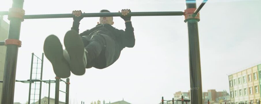 Arc shot of athlete performing front lever on parallel bars while exercising outdoors at workout playground