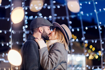 Romantic Christmas lovers kissing on the street on New Year's eve. A young romantic couple kissing on the street surrounded by Christmas lights on Christmas eve.