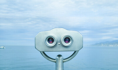 Public binocular on the seashore, close up. Coin-operated binocular viewer on blue sky background....
