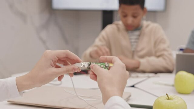 Close-up of child hands plugging in USB cord into flash drive with no body, microchip visible, secondary school students experimenting in classroom
