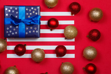 American flag composition with blue gift decorated with glittering stars and christmas tree decorations on red background. Merry christmas and happy new year concept..