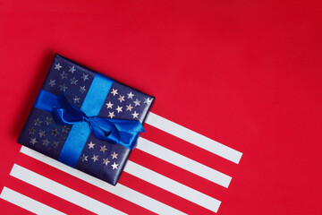 American flag composition with blue gift decorated with glittering stars on red background. Flat lay, top view, copy space. Minimalistic stylish background for design free space.