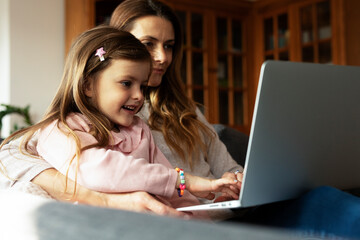 Cheerful little girl using laptop. Beautiful girl watching cartoon with mom.