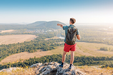 A happy male traveler with a backpack climbed to the top of Mount Shikhan in Bashkiria and admires the views