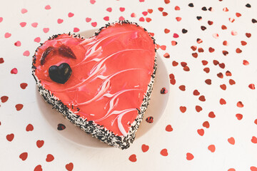 Valentines Day heart shaped cake with chocolate and strawberries on plate, white with red hearts confetti background. Festive dessert for date, anniversaries and party concept. Close up, copy space