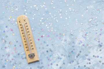Thermometer shows low plus temperature and Christmas decoration on white and blue with stars festive background. Winter and holiday weather concept, copy space