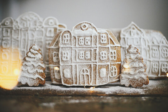 Christmas gingerbread houses and tree in snow on rustic wooden table with golden lights. Christmas cookies village scene. Atmospheric moody image. Winter holiday traditions. Merry Christmas!