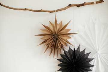 Stylish Christmas stars hanging on wooden branch on white wall. Modern festive scandinavian decor...