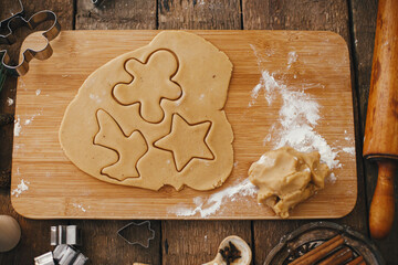 Gingerbread dough with christmas star, reindeer, gingerbread man  shape on wooden board. Top view. Atmospheric Moody image. Making traditional christmas gingerbread cookies on rustic table