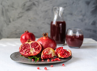 pomegranates on the plate with leaves, juice backside, grey background and white table