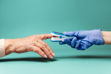Doctor puts an oximeter on the index finger of an senior woman. Hands close-up. The concept of...