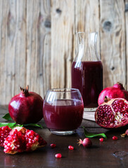 pomegranates juice and fruits with leaves, wooden background