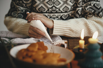 Hands decorating christmas gingerbread cookie star with icing on rustic table with candle, napkin, decorations. Atmospheric moody image. Woman making traditional christmas gingerbread cookies