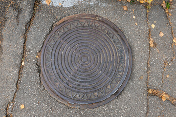 Old shabby round manhole cover on the city street