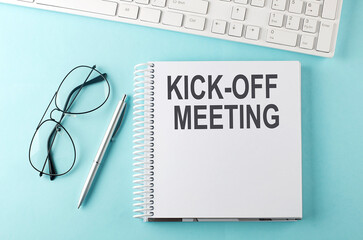 Keyboard, notebook,pen and glasses on the blue background , text KICK OFF MEETING
