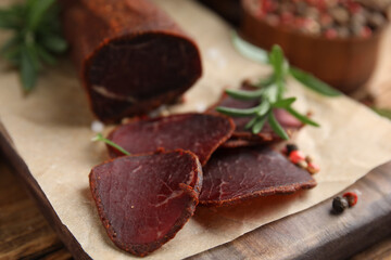 Delicious dry-cured beef basturma with rosemary and peppercorns on wooden table, closeup