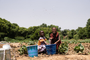 Two cute little black African girls sitting in a vegetable field playing with water