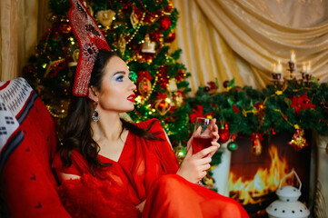 New Year's portrait. woman in a red dress drinks wine from a glass near the new year tree