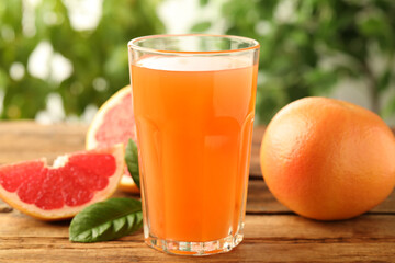 Glass of delicious grapefruit juice on wooden table against blurred background