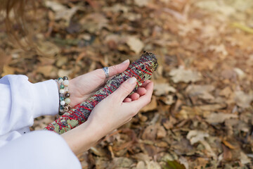 Female hands with bracelets hold a herbal fumigation twist when meditating outdoors. A bunch of field herbs for relaxation exercises, yoga, aromatherapy. Close-up. Copy space