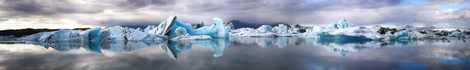Ultra wide panorama of the Jokulsarlon Glacial lagoon, Southern Iceland. Mirror reflection of the blue ice icebergs.