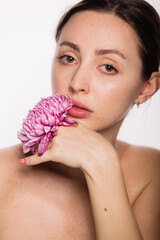 Pretty woman with flower in her hands near the face naked shoulders clear skin. Skin care and Spa concept on white background. Woman looking at camera