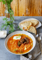Sour cabbage soup with ingredients in a white plate, wooden background and grey table