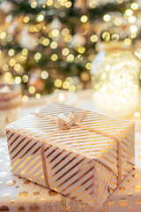 A lot of packing handmade gift boxes lying on the table near Christmas tree in the midst of golden lights, glowing garland, candle. Soft focus. Vertical ratio