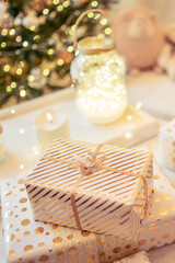 A lot of packing handmade gift boxes lying on the table near Christmas tree in the midst of golden lights, glowing garland, candle. Soft focus. Vertical ratio