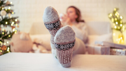 Woman sitting on couch near christmas tree. Female legs, feet in winter woolen socks putting on the...