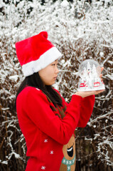 An asian korean girl in red jumper and sants hat holding a snow globe in the snow