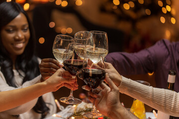 holidays, party and celebration concept - multiethnic group of happy friends having christmas dinner at home and drinking wine